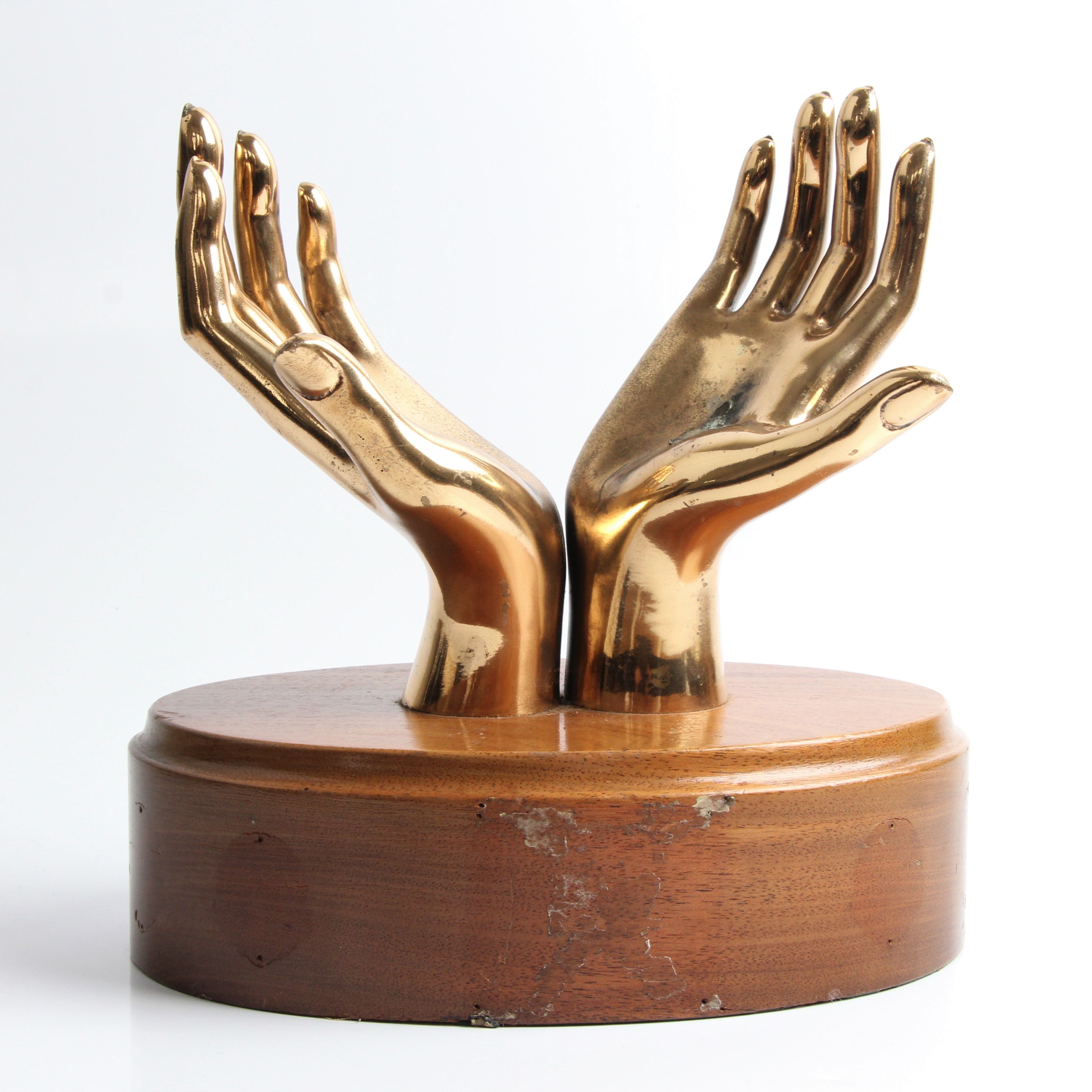A brass trophy in the form of lifted hands, on wooden base, approx. height 25cm. IMPORTANT: Online