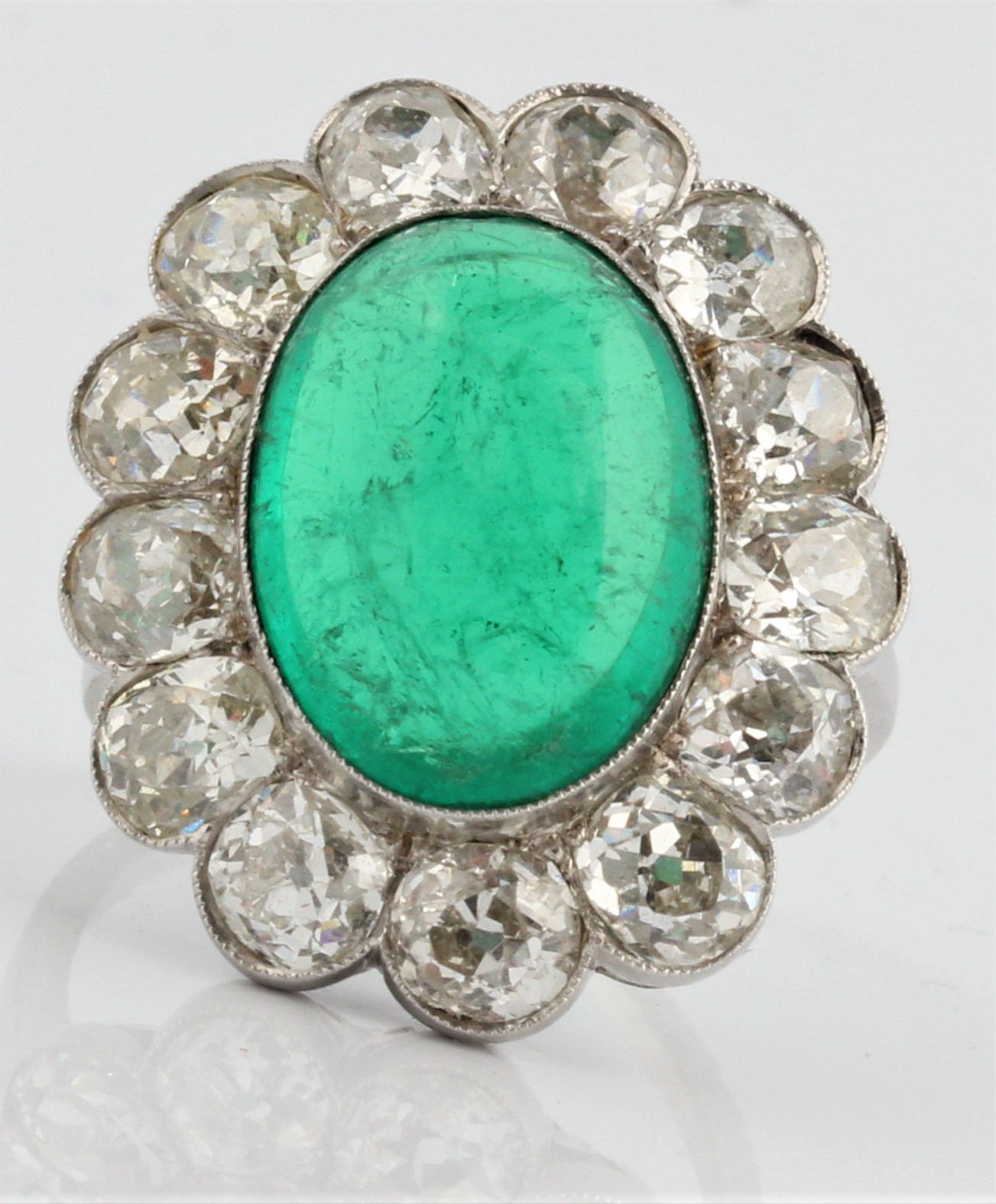 An emerald and diamond cluster ring, set with a central oval emerald cabochon, measuring approx.