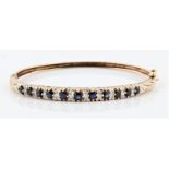 A hallmarked 9ct yellow gold sapphire and diamond hinged bangle, set with 11 graduated round cut