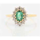 A hallmarked 18ct yellow gold emerald and diamond cluster ring, set with an oval cut emerald,