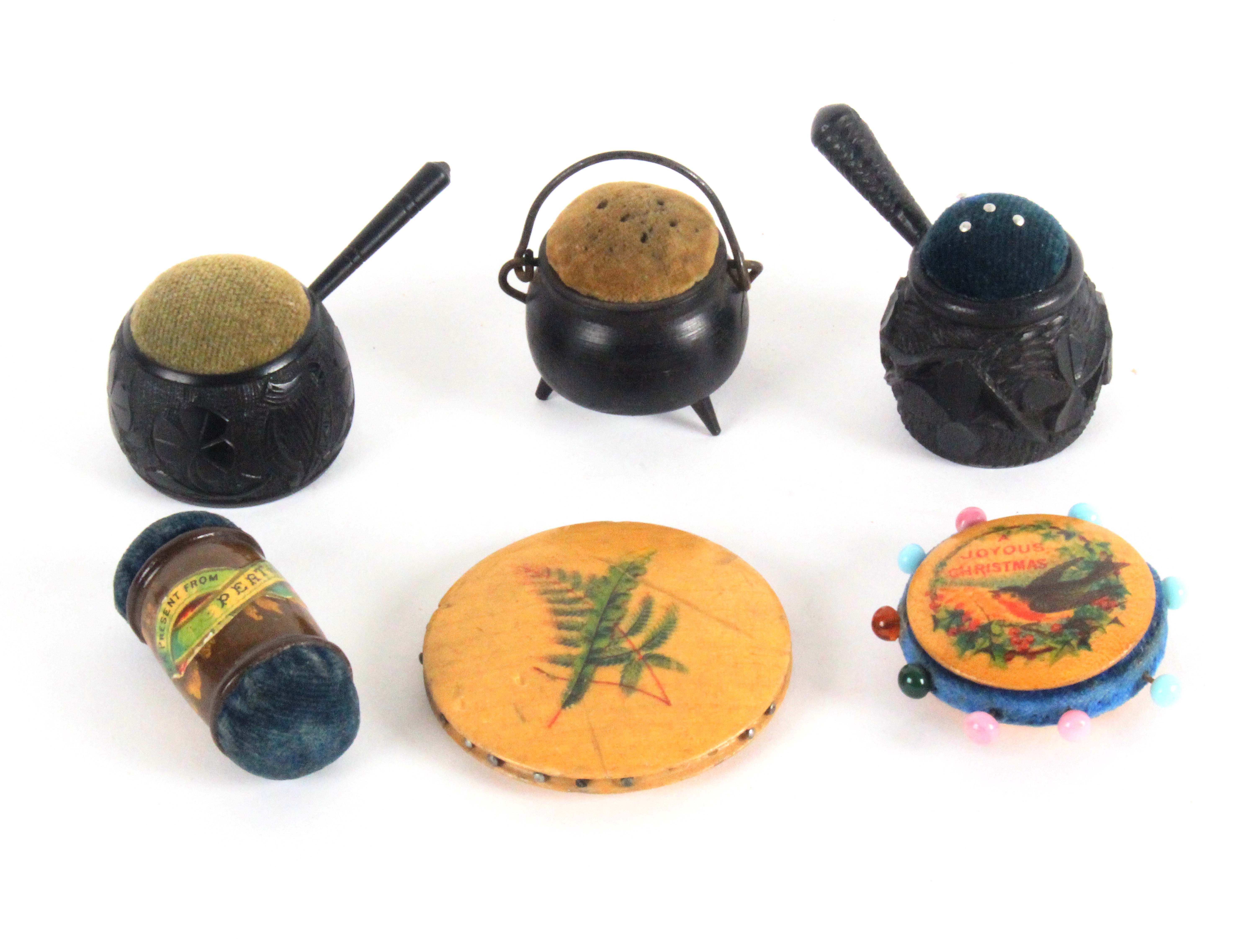 Six pin cushions, comprising two carved bog oak saucepans and a similar cauldron, and three