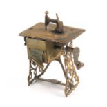 A scarce novelty brass tape measure in the form of a treadle sewing machine, complete printed tape