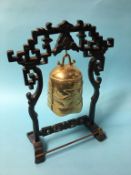 An Oriental brass hanging bell, with carved wood stand