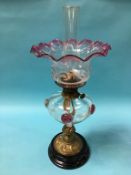 An Edwardian oil lamp, with flared cranberry shade and clear glass reservoir