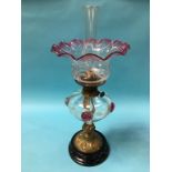 An Edwardian oil lamp, with flared cranberry shade and clear glass reservoir