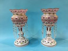 A pair of Victorian cranberry vases, with overlaid white glass lustres, decorated with rose heads