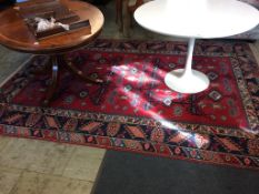 A red ground Caucasian style rug, with hooked medallions and main midnight blue geometric border.