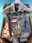 A denim jacket with numerous cap and shoulder badges and medals etc.