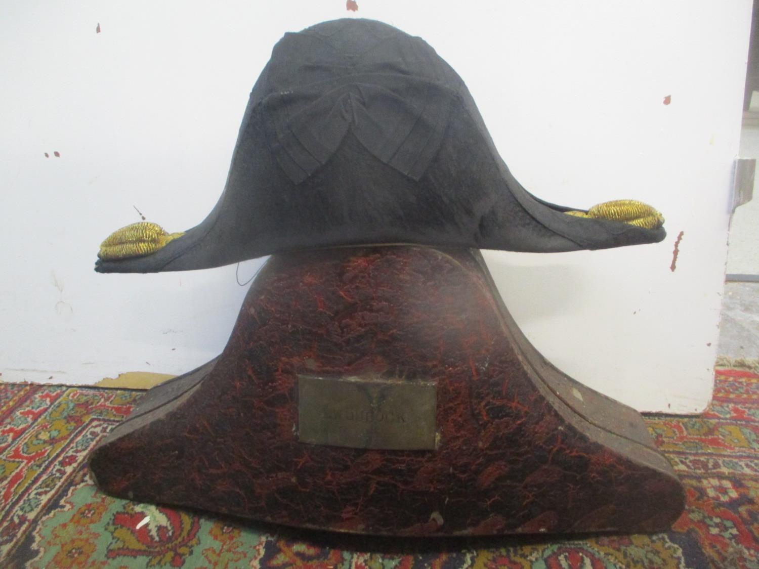 A 19th century Naval bicorn hat, with gilt braid, in a painted metal carrying case, the brass plaque