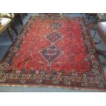 A Middle Eastern red ground rug having three motifs and multiguard borders 293cm x 222cm