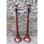 A pair of Arts and Crafts style floor standing mahogany candle holders, with tapered faceted