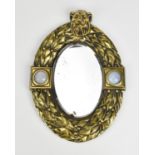 An Art Deco Grays brass wall mirror, of oval form with laurel leaf border, surmounted with a lion