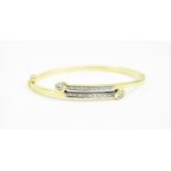 A yellow metal and diamond bangle, the front with overlapping rows of diamond accents with a