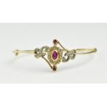 A yellow metal, ruby and diamond bangle with central floral cluster centered with oval ruby with