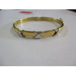 A gold coloured metal bangle with crossover ornament