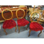 A set of three Victorian walnut balloon back chairs with carved crest rail, button upholstered red