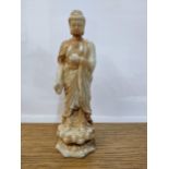 A Chinese off white and rust jade coloured statue of a man holding a bowl on a lotus base