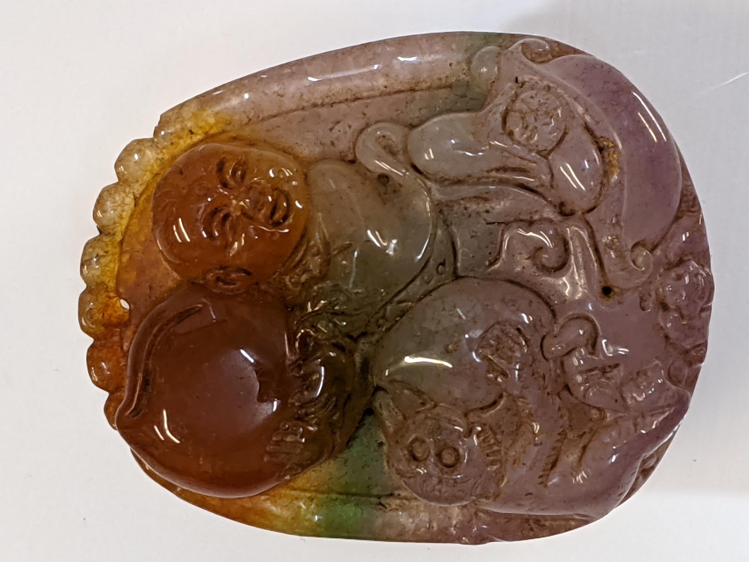 A Chinese pink, green, brown jade pendant carved with a child, fruit and a monkey, 5cm x 4cm