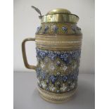 A Doulton Lambeth stoneware jug having a brass lid and decorated with raised floral detail, numbered