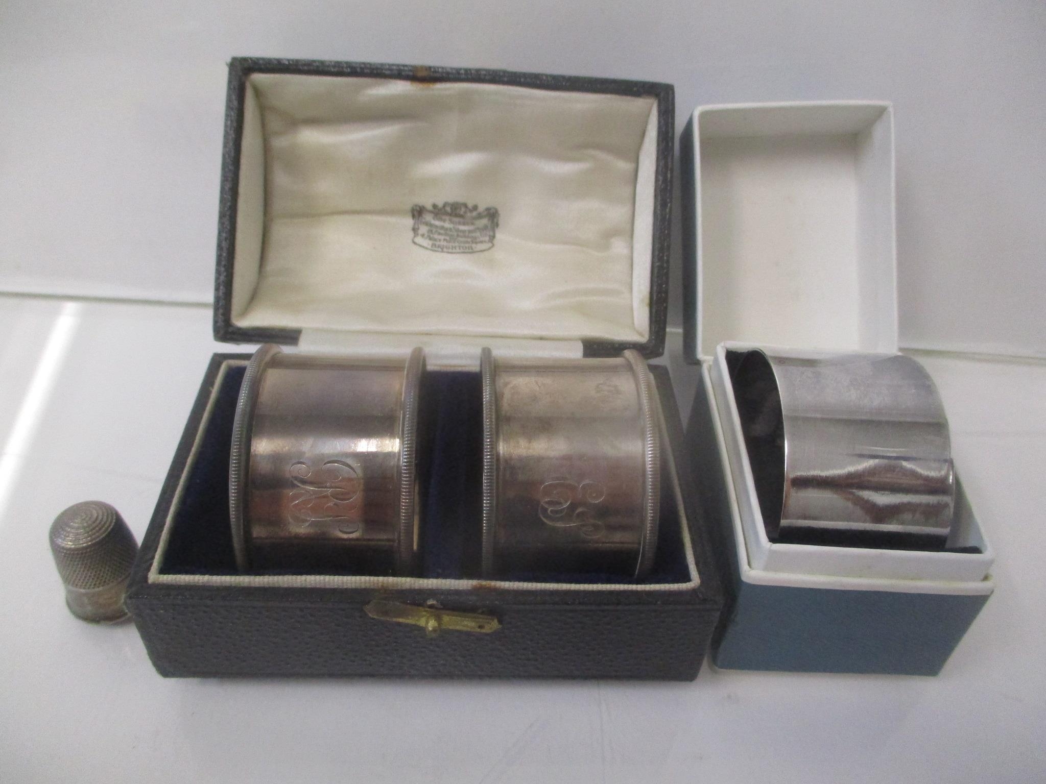 A pair of silver napkin rings, boxed, a napkin ring box and a thimble, 65g