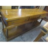 A reproduction oak sideboard having three drawers with open shelf below and on a plinth base, 91cm h