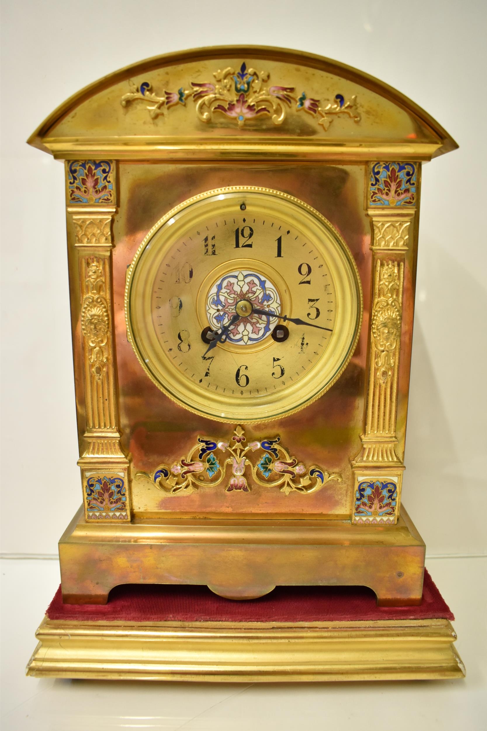 An early 20th century brass mantle clock on a gilded treen stand, the arched top case with floral