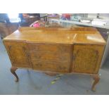 A 1950's walnut breakfront sideboard having three drawers flanked by two cupboard doors standing