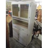 A 1950's white painted kitchen cabinet with glazed and solid doors, drawers and an up and over door,