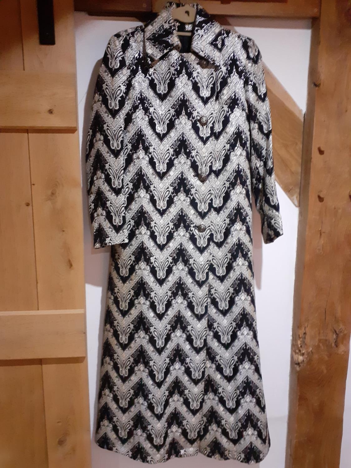 A Retro full length coat having a black ground with white chevron design, silver coloured thread