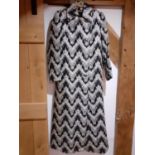 A Retro full length coat having a black ground with white chevron design, silver coloured thread