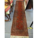 A hand woven red ground Bokhara runner with central motifs and tasselled ends