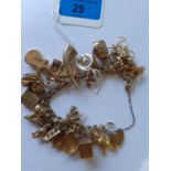 A 9ct and yellow metal charm bracelet having 25 charms and a hear locket catch with safety chain,