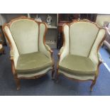 A pair of 20th century French walnut framed wing back armchairs, with a carved crest, scrolled