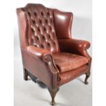 A Buttoned Upholstered Leather Wing Armchair with Brass Studwork and Short Cabriole Supports