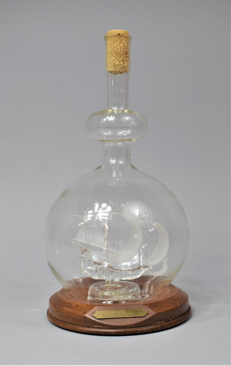 A Contemporary Glass Ship in a Bottle on Circular Wooden Plinth, 28cm high