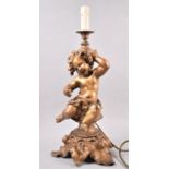 A Gilt Painted Spelter Table Lamp in the Form of a Seated Cherub Set on Naturalistic Foliate Stand