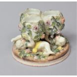 A German Porcelain Novelty in the Form of Three Eggs Supported by Cherubs, 13cm Diameter