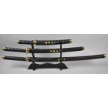 A Reproduction Graduated Set of Three Samurai Katanas on Wooden Stand, Longest 90cm