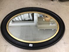 A VICTORIAN EBONISED BEVELLED EDGE WALL HANGING OVAL MIRROR WITH GILT BORDER 91CM X 65CM