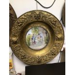 AN EARLY BRASS SURROUND WALL MOUNTED HANDPAINTED CERAMIC CHARGER, 59CM DIAMETER