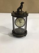 AN OMEGA MECHANICAL CLOCK WITH A DOG FINIAL TO THE TOP IN A GLASS CASE, 14CM