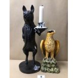 A RESIN FIGURE OF AN EAGLE WITH AN EBONISED PIG CANDLE HOLDER DRESSED IN FORMAL ATTIRE