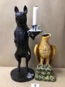 A RESIN FIGURE OF AN EAGLE WITH AN EBONISED PIG CANDLE HOLDER DRESSED IN FORMAL ATTIRE