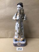 A JAPANESE PORCELAIN FIGURE CARRYING A WHITE METAL BRACELET RED CHARACTER MARK TO BASE, 29CM