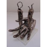 A surreal silvered metal sculpture of a hand supporting two figurines of a male and a female mounted
