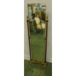 A gilded metal rectangular cheval mirror with urn finials to the sides on four scroll supports,