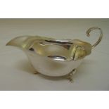 A silver sauce boat, oval with crimped edge and flying double scroll handle on three scroll feet,