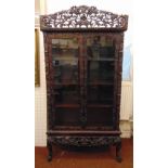 A Chinese rectangular hardwood glazed double door display cabinet, profusely carved and pierced with
