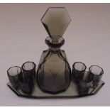 An Art Deco style smokey glass decanter with drop stopper, tray and six liqueur glasses