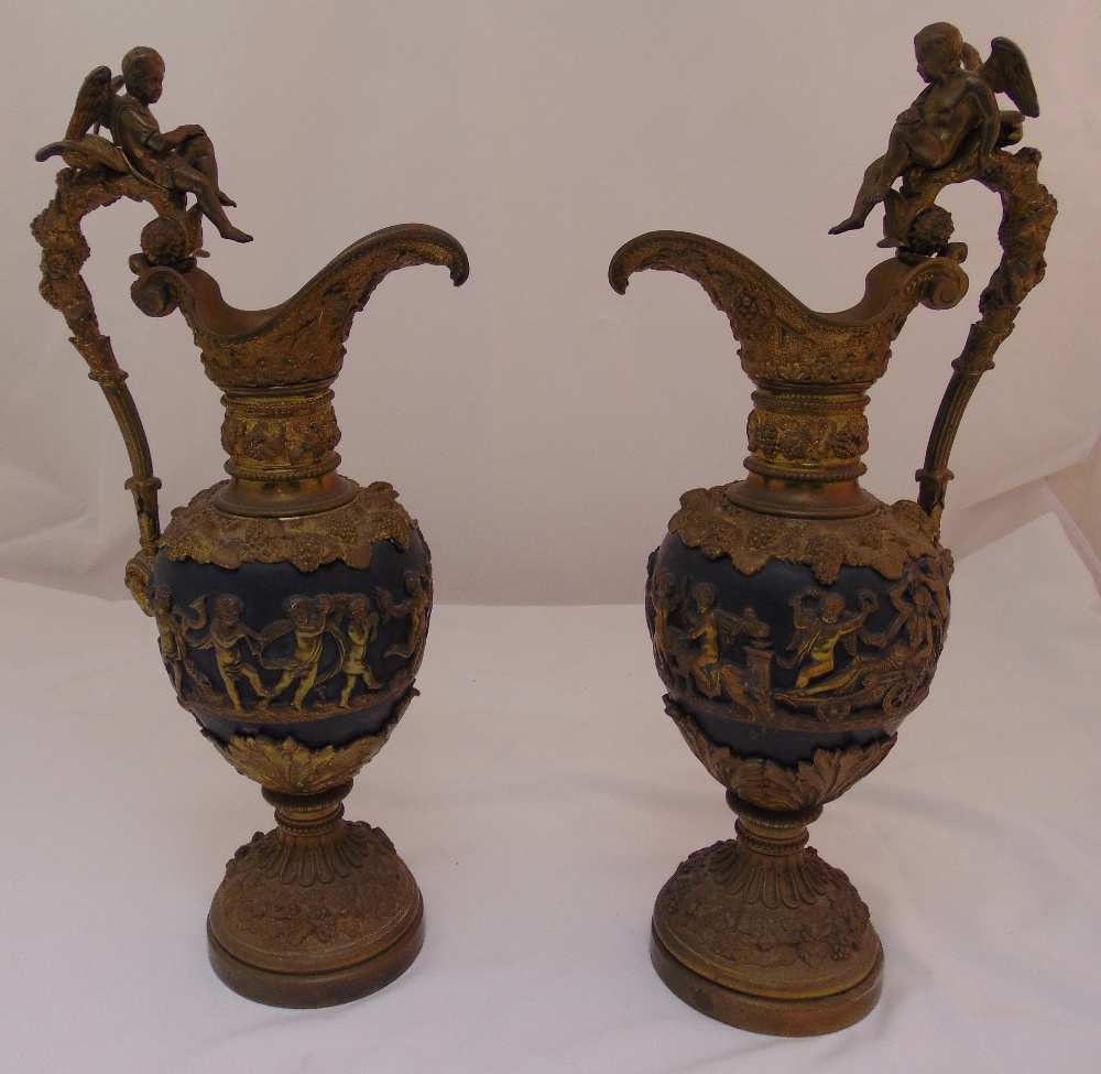 A pair of gilded metal ewers decorated with classical figures, vine leaves and grapes, the scroll